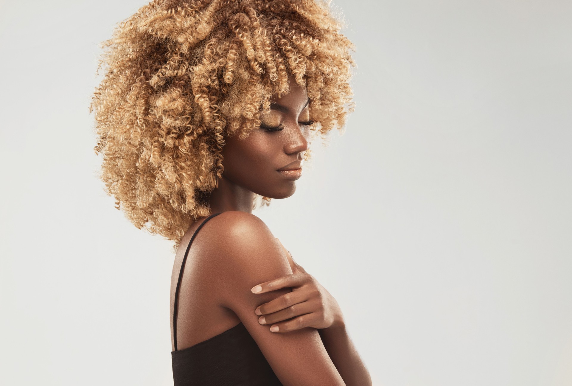 Model with vibrant melanin-rich skin tone is demonstrating dyed dense curly hair. Afro hair. Afro beauty.